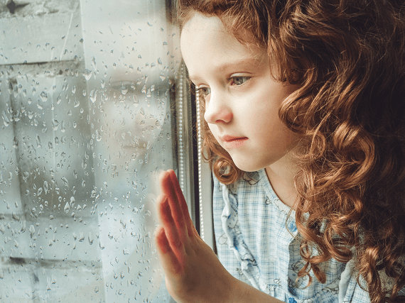 Dievča pri okne pozoruje dážď